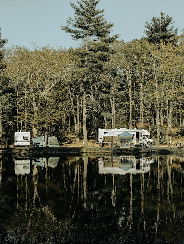 why-choose-us-02 Peaceful lakeside camping scene with RVs, tents, and reflections in the water, surrounded by trees.