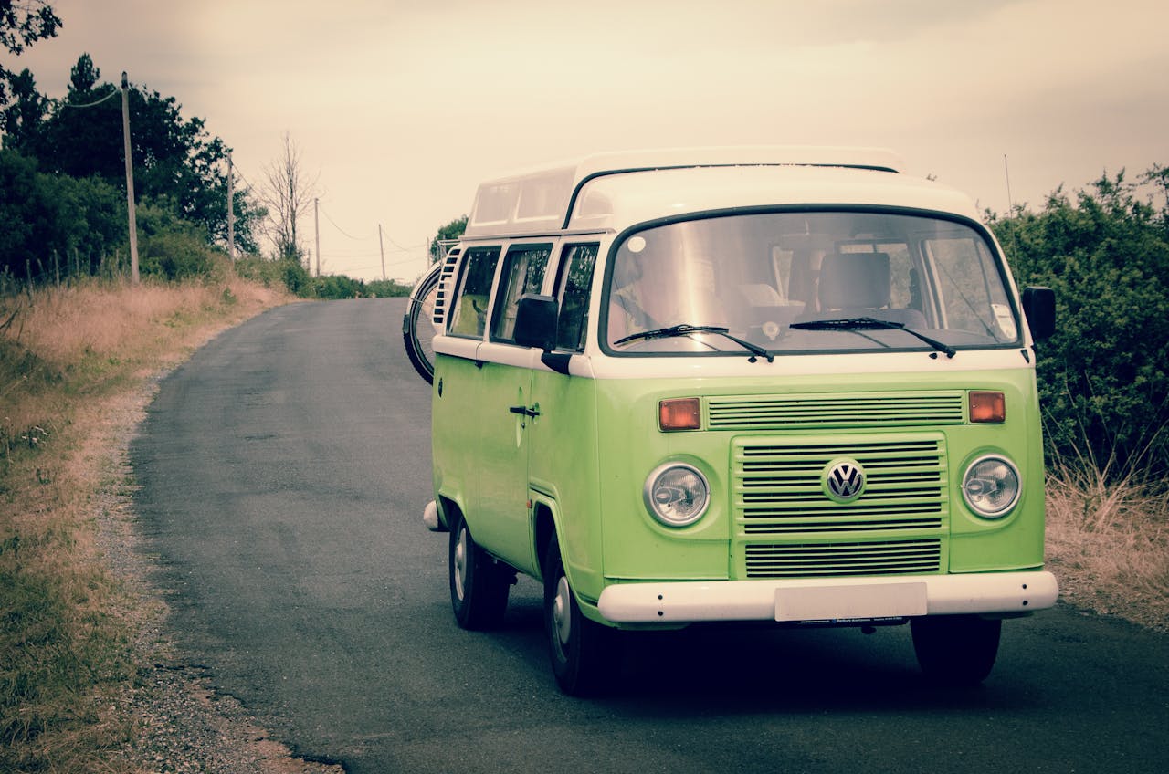 why-choose-us-01 Classic green Volkswagen campervan driving on a quiet country road, perfect for road trips and adventure in nature.