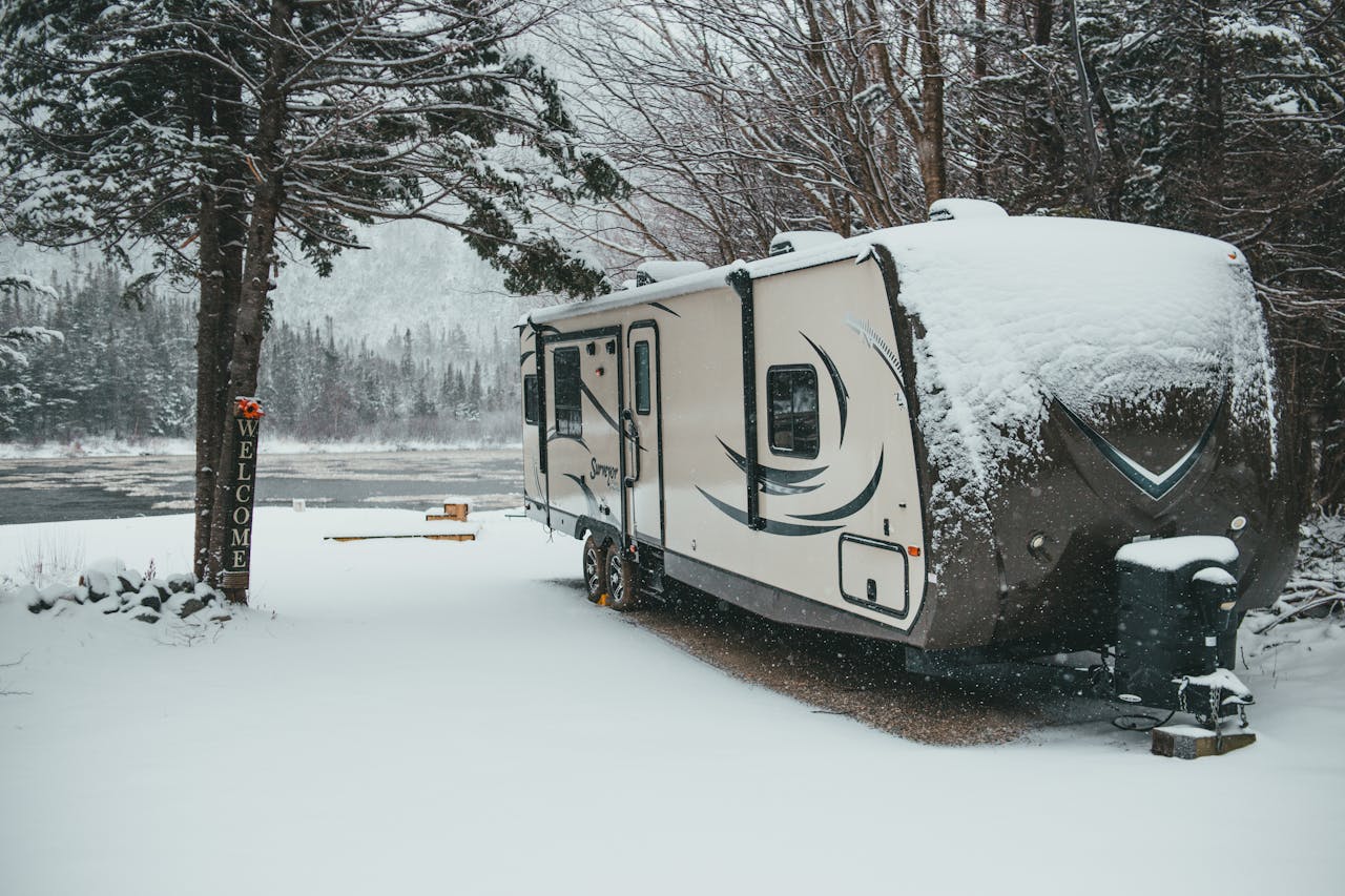 our-story-01 Travel trailer covered with snow placed on shore near river in winter forest in countryside in daylight